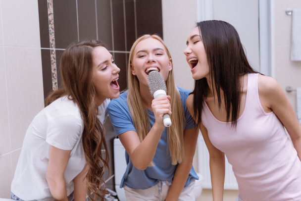 multiethnic friends singing in bathroom with round comb - Photo, Image