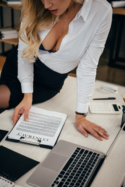 cropped image of seductive woman sitting on table and reading working contract - Фото, изображение