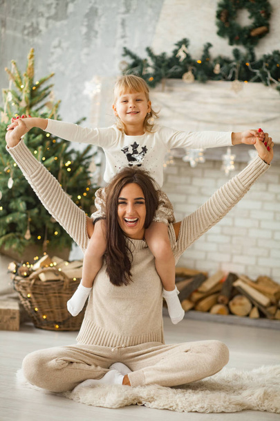 Madre e hija pequeña se están divirtiendo y jugando contra el fondo del árbol de Navidad y decoraciones
. - Foto, imagen