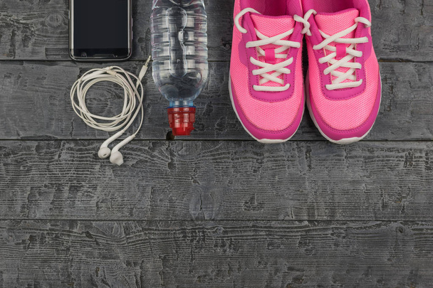 Belos tênis rosa, fones de ouvido, água e maçãs em um piso escuro de madeira. Vista de cima
. - Foto, Imagem