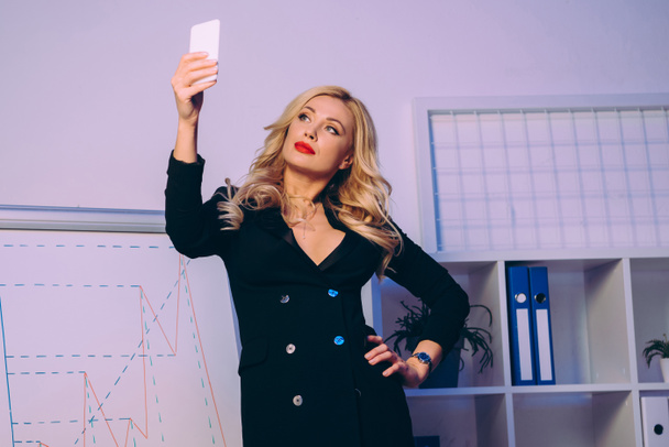 Verführerische Frau macht Selfie mit Smartphone in Diagrammnähe - Foto, Bild
