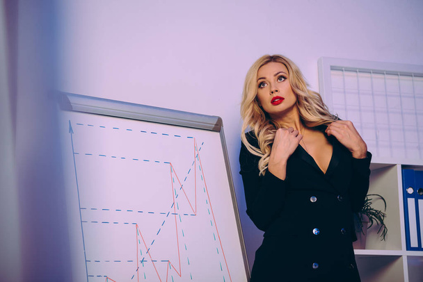 seductive woman standing in jacket near diagram chart and looking away - Fotografie, Obrázek