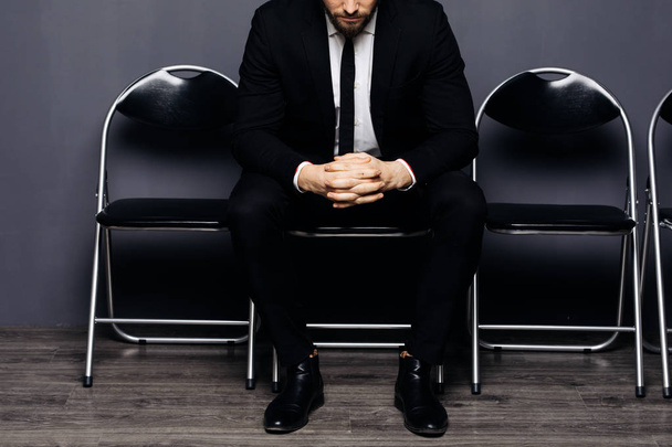 Крупным планом скрещенных рук молодого красавца, сидящего на стуле и ожидающего своей очереди в офисном зале
 - Фото, изображение