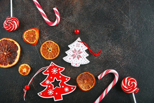 Christmas attributes. Caramelized oranges, fir branches and candy cane on dark background, Selective focus - Foto, Imagen