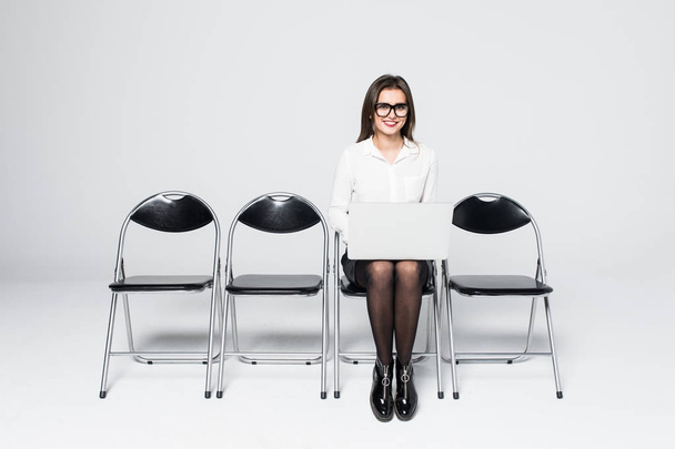 mladý, usměvavý office pracovník žena sedí na židli dřevěnou podlahu pomocí mobilní přenosný počítač připravit rozhovor setkání soubor izolované na bílém - Fotografie, Obrázek