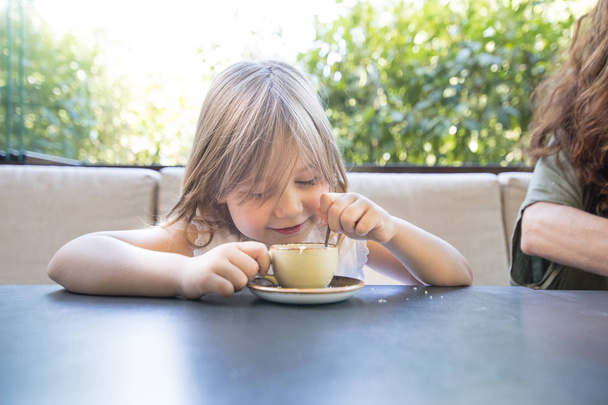 klein kind lacht en spelen met koffiekopje en lepel - Foto, afbeelding
