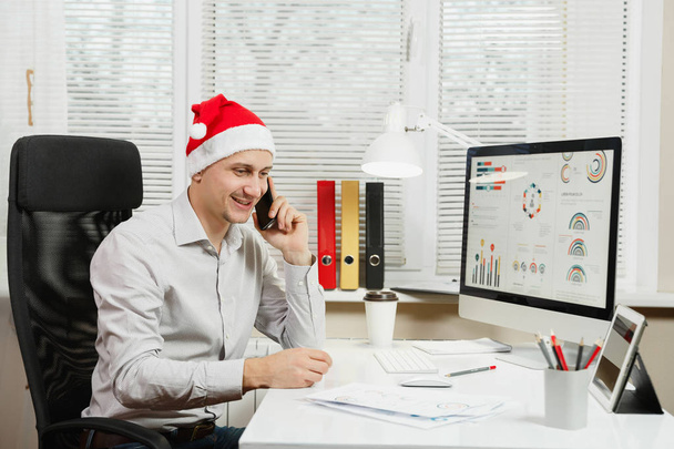 Красивый бизнесмен в рубашке и красной рождественской шляпе сидит на
  - Фото, изображение