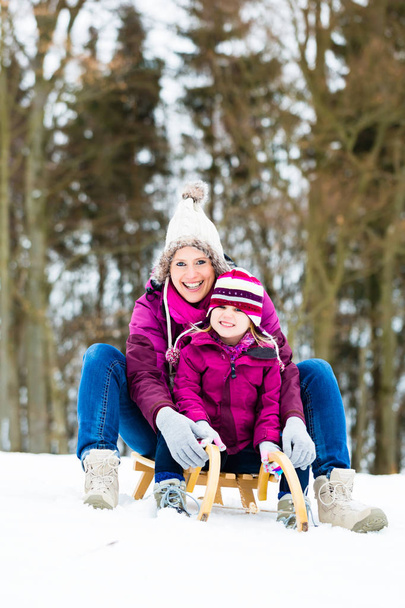 Жінка і дочка на санчатах взимку
 - Фото, зображення