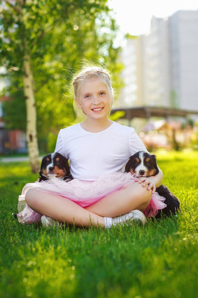 little blonde girl hugging cute puppies sitting on green grass - Photo, Image