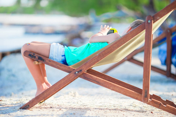 Αξιολάτρευτο κοριτσάκι χαλαρώνοντας σε πολύχρωμα ξύλινη καρέκλα στην παραλία κατά τη διάρκεια των θερινών διακοπών - Φωτογραφία, εικόνα