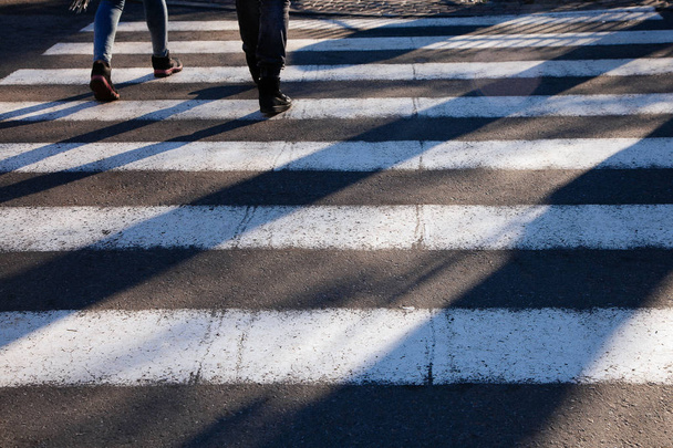 Close-up van zebrapad voorgrond voetgangers lange schaduwen junction straat voeten - Foto, afbeelding