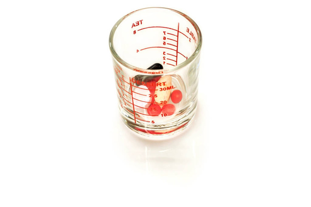 Pilules rouges et comprimés en médecine mesurant tasse en verre pour prêt à isoler le patient sur fond blanc et faire avec des chemins
. - Photo, image