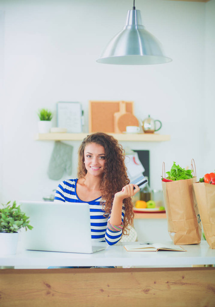 Smiling young woman with coffee cup and laptop in the kitchen at home. Smiling young woman - Foto, Bild