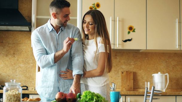 Happy young couple in the kitchen. Handsome man meet and feed his girlfriend early morning - 写真・画像