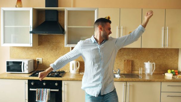 Όμορφος νεαρός αστείος άνθρωπος Χορεύοντας στην κουζίνα στο σπίτι το πρωί και να διασκεδάσετε στις διακοπές - Φωτογραφία, εικόνα