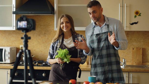 Young attractive couple shooting video food blog about cooking on dslr camera in the kitchen - Photo, image