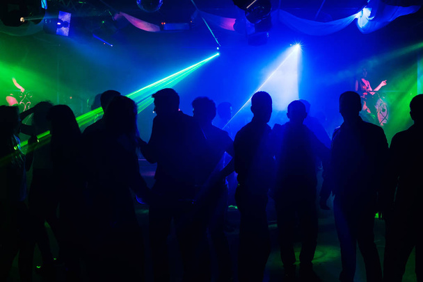 people silhouettes on dance floor of night club to laser projectors - Photo, Image