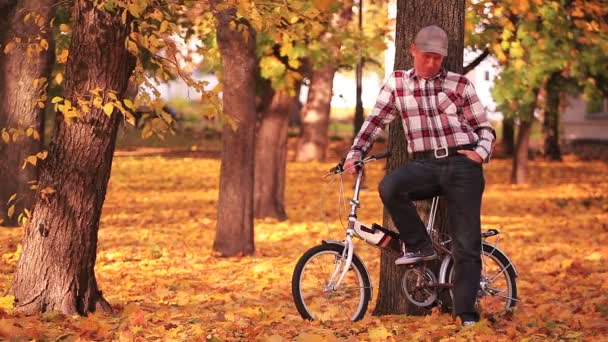 Volwassen man staan in de buurt van kleine fiets in herfst park met gele bomen - Video