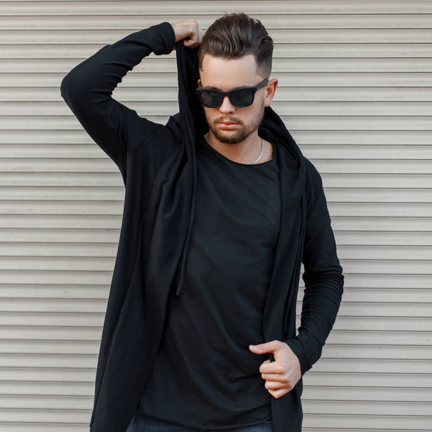 Fashionable handsome man in a black hoody with sunglasses posing near a metal wall - Photo, Image