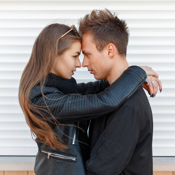 Hermosa pareja en un abrazo en chaquetas negras de moda cerca de la pared blanca
  - Foto, Imagen