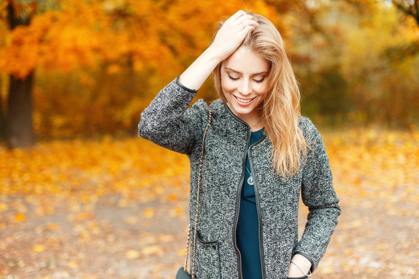 Beautiful young happy woman in fashionable autumn clothes walking in a park with yellow foliage - Photo, Image