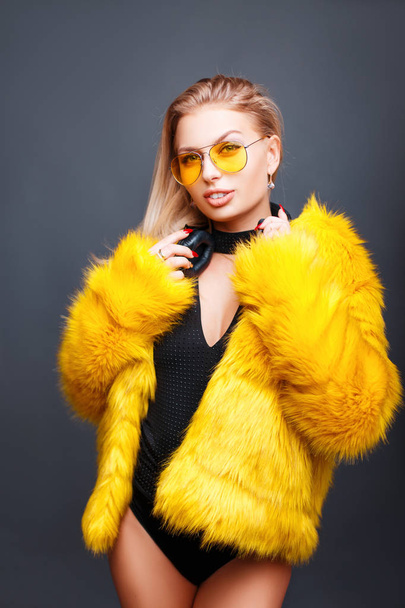 Fiatal modell egy nő Dj napszemüveg és divatos sárga bundát a szürke háttér - Fotó, kép