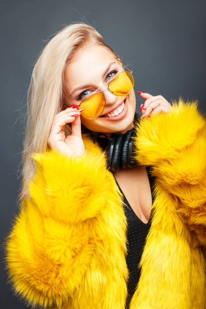 Щаслива красива ді-джея дівчина з посмішкою з модними сонцезахисними окулярами в стильній жовтій шубці на сірому фоні
 - Фото, зображення