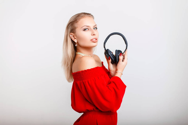 Belle jeune fille dans des vêtements rouges élégants tient écouteurs et posant sur un fond gris
 - Photo, image
