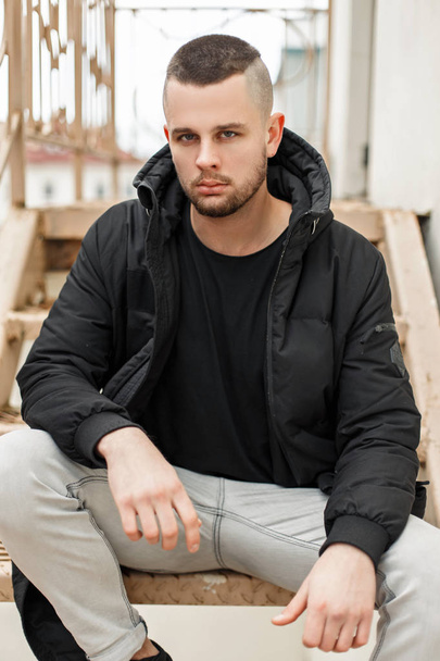 Pohledný mladý model muže s krátký střih v módní zimní bunda sedí na schodech - Fotografie, Obrázek