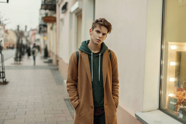 Guapo joven y elegante hombre con un abrigo de otoño vintage cerca de la tienda con bombillas
 - Foto, imagen