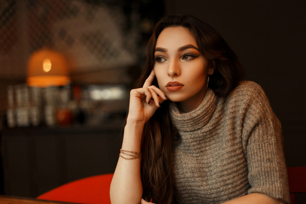 Joven hermosa mujer en un suéter de punto elegante se sienta en un café y sueña
 - Foto, Imagen