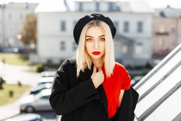 Piękny modny blond dziewczyna w modne jesienne czarny płaszcz z beret pozowanie w mieście na słoneczny dzień - Zdjęcie, obraz