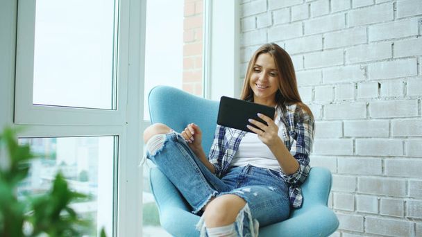 Young happy woman have online video chat using digital tablet computer sitting on balcony in modern loft apartment - Photo, image