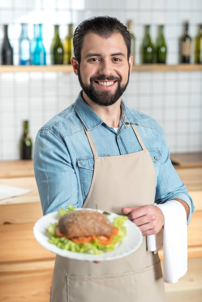 Excited enthusiastic waiter smiling while showing a tasty meal - Φωτογραφία, εικόνα