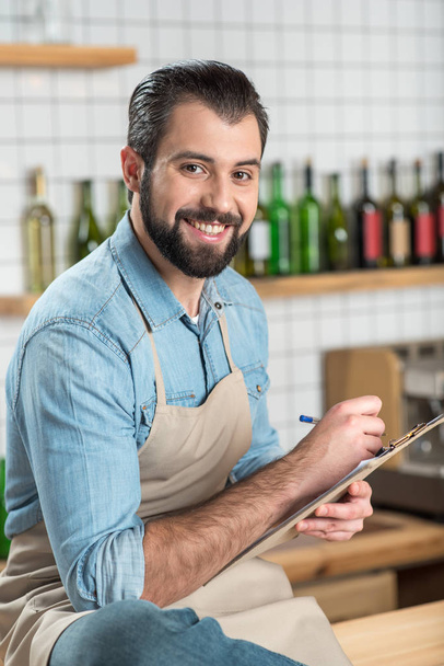 Creative young man smiling while writing a menu for a cafe - Zdjęcie, obraz