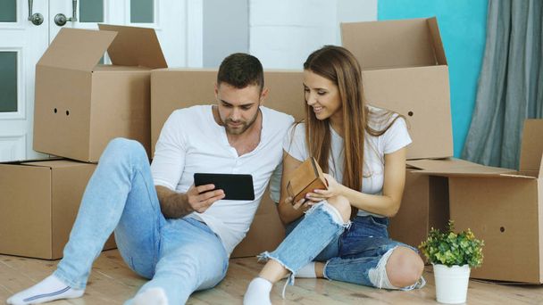 Young couple sitting on floor using tablet computer after reloction in their new home - Photo, image