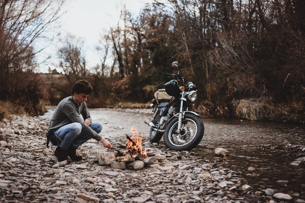 Seitenansicht eines Reisenden am Lagerfeuer durch geparktes Motorrad - Foto, Bild