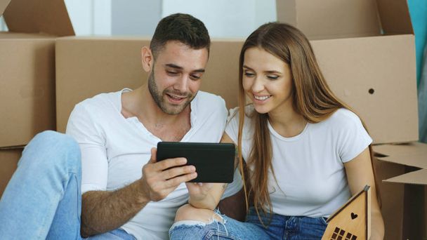 Young couple sitting on floor using tablet computer after reloction in their new home - Foto, afbeelding