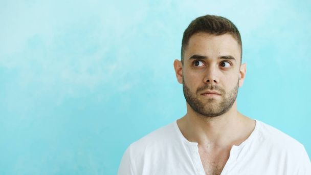 Portrait of young handsome man grimacing into camera and show different emotions on blue background - Photo, Image