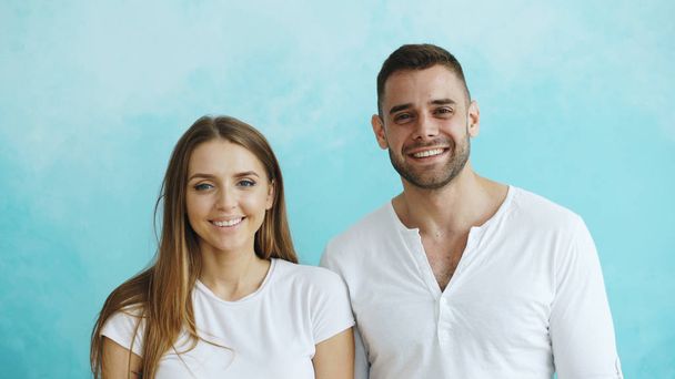 Portrait of young happy couple smiling and laughing into camera on blue background - Φωτογραφία, εικόνα