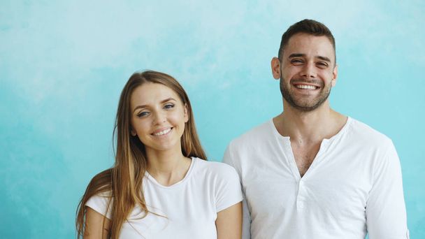 Portrait of young happy couple smiling and laughing into camera on blue background - Foto, Bild