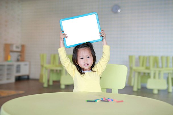 Cute asian child girl holding empty white blackboard in kids room. - Valokuva, kuva