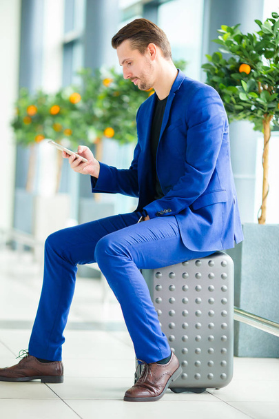 Молодий чоловік з мобільним телефоном в міжнародному аеропорту чекає на посадку
 - Фото, зображення