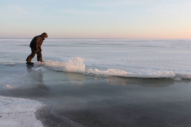 Man  walking through a crack on thin ice on a frozen river - Фото, изображение