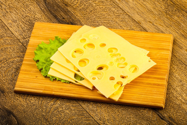 Szeletelt sajt saláta levelek fölött a fából készült háttér - Fotó, kép