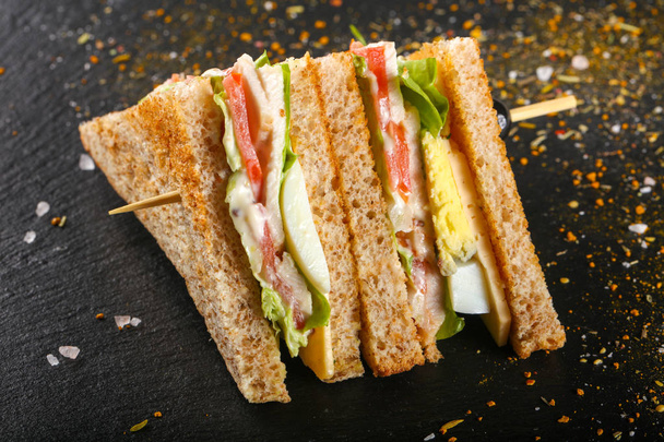 Club sandwich with meat, cheese and vegetables over wooden background - Photo, Image