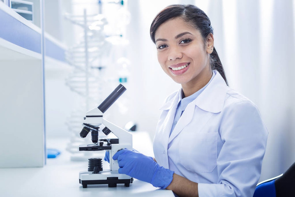 Delighted smart woman sitting in front of the microscope - Φωτογραφία, εικόνα