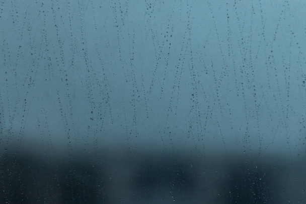 Фон з дощовими краплями, що спускаються зі скла за вікном
. - Фото, зображення