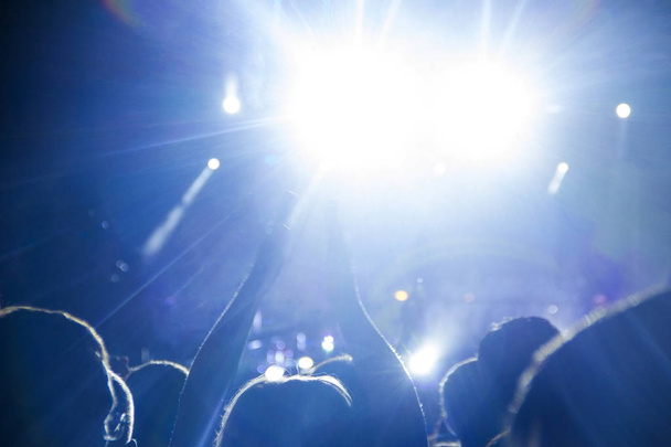 Люди дивляться концерт під відкритим небом і плескають руками в яскраво-блакитне світло
. - Фото, зображення