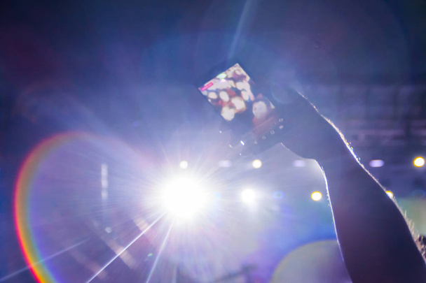 Το χέρι του άνδρα κάνει μια selfie κατά τη διάρκεια μια υπαίθρια συναυλία. Είναι θολή. - Φωτογραφία, εικόνα
